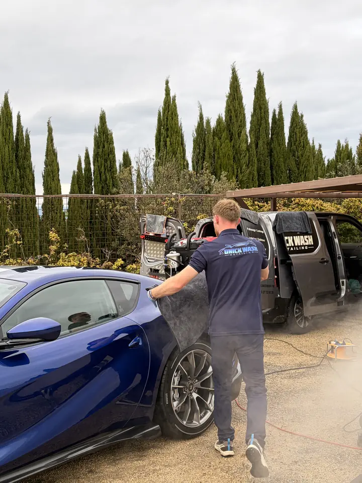 Membre de l'équipe Unick Wash essuyant une Ferrari 812 Competizione bleue, camion atelier derrière