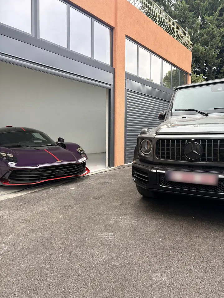 Aston Martin Valhalla violette et Mercedes G63 devant un garage