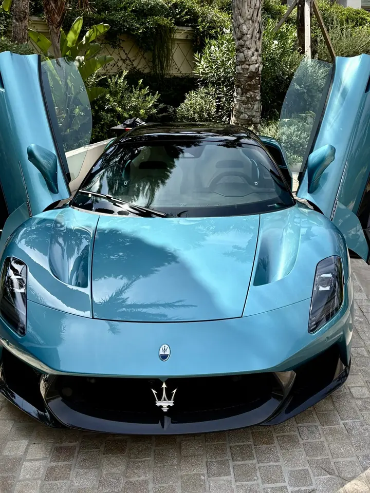 Maserati MCPura bleu-vert, portes papillon ouvertes, vue de face devant une villa