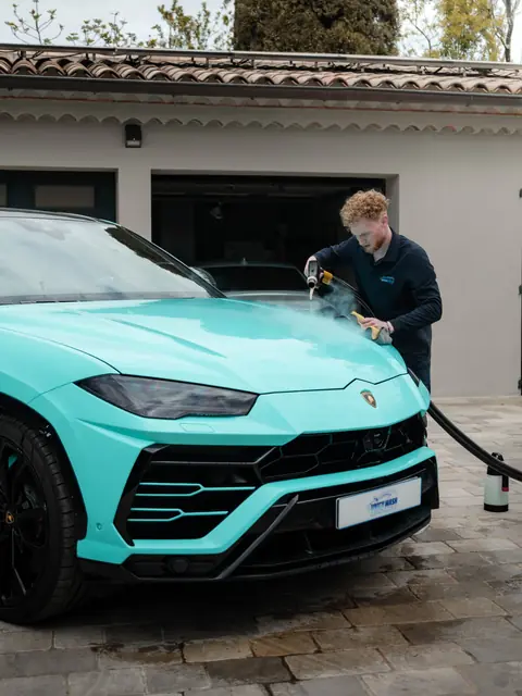 Un membre de l'équipe nettoie une voiture à la vapeur devant un garage